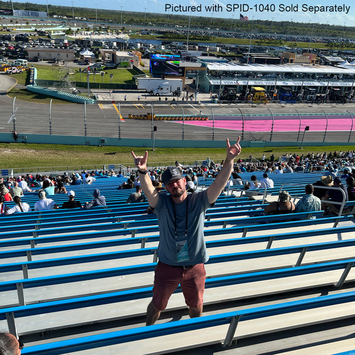 A man stands with arms raised on blue stadium bleachers, wearing a 25 Pack Bulk Double-Ended Lanyards with Bulldog Clips on Each Side Assorted Colors around his neck, with a racetrack and spectators in the background.