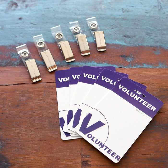 Five USB drives and four 5 Pack - Purple Heavy Duty Plastic Volunteer Badges with Clothing Friendly Clip are placed on a worn wooden surface. Sold by Specialist ID.