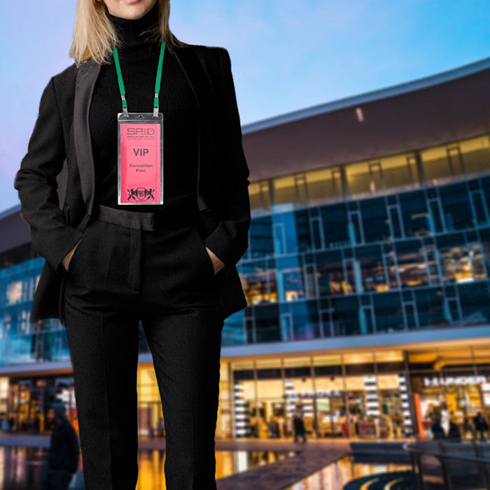 A person in a black outfit with hands in pockets, wearing a VIP badge on a 5 Pack Double Ended Lanyards with Bulldog Clips - Comfortable Premium Economy Neck Strap Badge Holder for Events around their neck, stands in front of a modern, glass-fronted building at dusk.