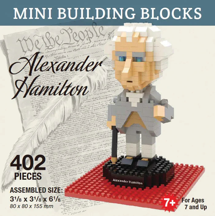 The Alexander Hamilton Mini Blocks set comes in a lightweight, glossy, and colorful cardboard box. The exterior features printed graphics, including a rendering of the assembled figure posed on a black base with a red platform beneath it. The product name appears in bold black script over a soft gray background depicting the U.S. Constitution and a white quill pen, tying the design to Hamilton’s legacy.