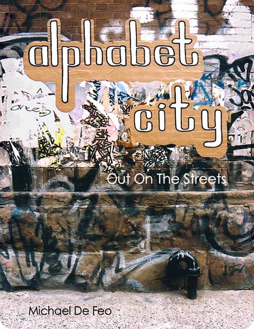 The book cover features a photograph of a brick wall covered in colorful graffiti, dominated by brown and tan tones with accents of blue, yellow, pink, black, and white. The title “Alphabet City” appears in bold white lettering over the artwork, with the subtitle “Out on the Streets” beneath it, reinforcing a gritty urban street aesthetic.