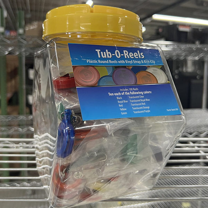 A clear plastic jar with a yellow lid labeled "Assorted Badge Reels TUB-O-REELS" containing assorted badge reels in various colors, displayed on a metal shelf. Sold by Specialist ID.