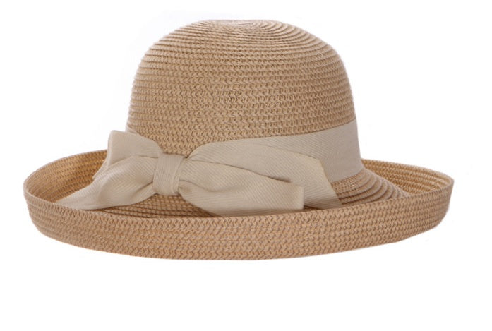 Backbow Roller Sunhat. Packable Straw Braid Roller Sunhat featuring a classic kettle-style upturned brim, and an adjustable drawstring inner band for a customized fit. The natural/cream woven straw hat is accented with cream grosgrain banding around the base of the crown and a prominent cream fabric bow at the back, shown against a solid white background.