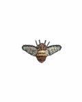 A small bee-shaped brooch with a rounded body and outstretched wings. The surface blends soft fabric with raised stitching, beads, and sequins, creating a gently textured feel with a subtle shimmer in shades of brown, blue, and black.The body is striped and slightly raised, with delicate wings extending outward. A smooth metal pin is attached to the back for fastening, and each handmade piece features slight variations in detail and finish.