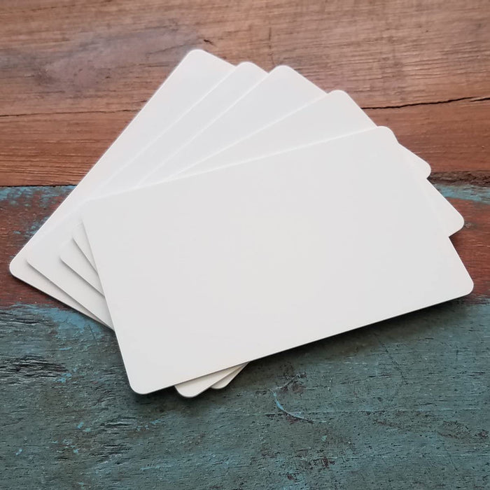 Stack of blank white CR80 PVC cards fanned on wood surface