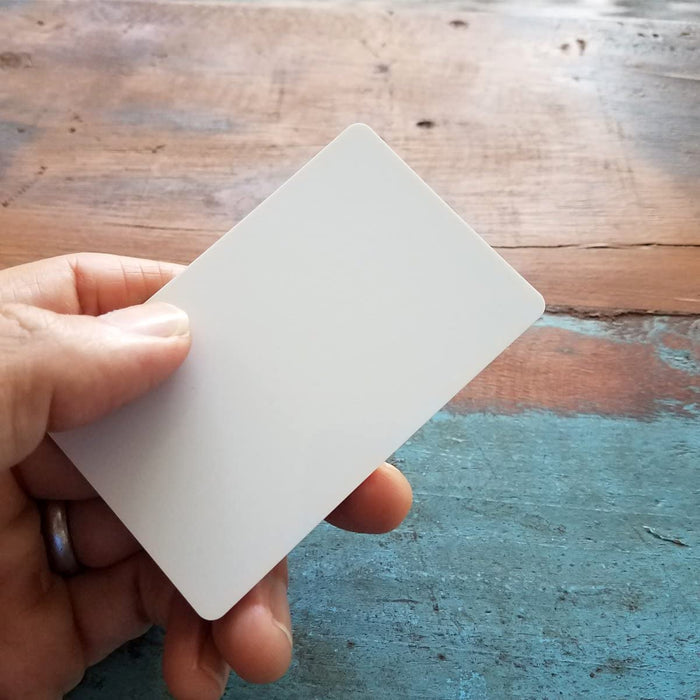 Hand holding blank white CR80 PVC card over rustic wood surface