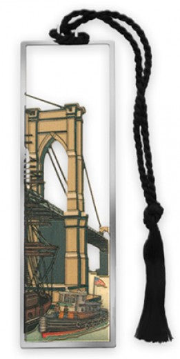 Brooklyn Bridge Bookmark shown against a white background. The bookmark features a black cord with a tassel and a rectangular silver-tone frame depicting the Brooklyn Bridge, with a mustard-colored Gothic arch, suspension cables, and a small red tugboat flying an American flag. Measuring approximately 4.5 inches long, the bookmark is intricately etched and cut out from solid brass, finished with polished, non-tarnishing silver plating.