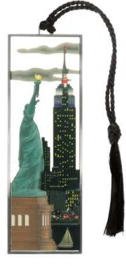 Featured against a white background, the Liberty and Empire State Metal Bookmark depicts a white sailboat on a dark blue harbor, with the Statue of Liberty in oxidized green and the Empire State Building glowing with yellow-lit windows. Gray horizontal clouds stretch across the nighttime sky. The colorful scene is framed by a silver-finished metal border and accented with a black tassel.