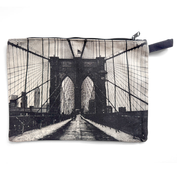 A soft, rectangular pouch in neutral canvas with a high‑contrast image in black, grey, and white. The Brooklyn Bridge stretches across the surface—its tall stone towers rise upward while fine cable lines fan out in all directions, creating a structured, web‑like pattern. The background is light and clean, making the dark lines of the bridge stand out clearly. A zipper runs along the top edge.