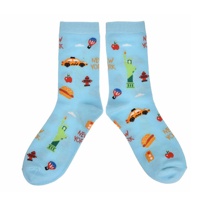 Featured against a white background, a pair of light blue NYC Cartoon Icon Socks decorated with playful illustrations of New York City favorites, including the Statue of Liberty, yellow taxis, hot dogs, fire hydrants, and other iconic city symbols. The colorful, cartoon-style design creates a fun and lively celebration of New York.