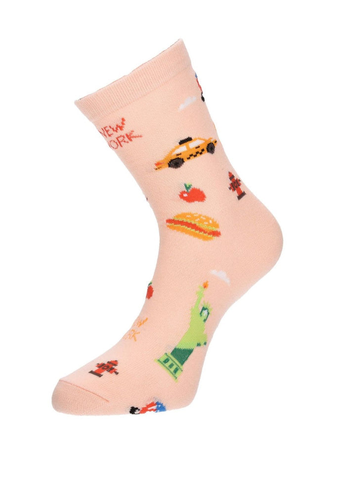 The image shows the peach/beige NYC Cartoon Icon Sock displayed on a mannequin foot. The sock is decorated with playful, colorful illustrations of New York City favorites, including the Statue of Liberty, yellow taxis, hot dogs, fire hydrants, and other iconic city symbols, as shown in the previous image.