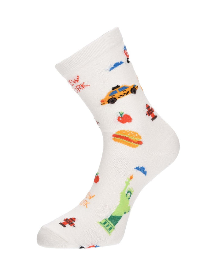 The image shows the white NYC Cartoon Icon Sock displayed on a mannequin foot. The sock is decorated with playful, colorful illustrations of New York City favorites, including the Statue of Liberty, yellow taxis, hot dogs, fire hydrants, and other iconic city symbols, as shown in the previous image.