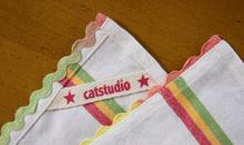The image shows a corner of the dish towel turned over, revealing the “catstudio” logo embroidered in red lowercase script, flanked by a small red star.
