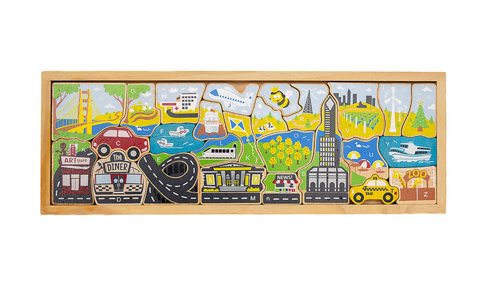 A long wooden A–Z puzzle with 26 chunky letter pieces showing city scenes like a skyscraper, skyline, taxi, museum, and bridge. The smooth, narrow tray has shallow cutouts that keep the pieces neatly in place. Thick rubberwood letters are easy to hold, painted in bright reds, blues, greens, and yellows over visible wood grain.
