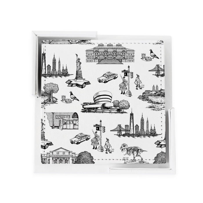 A set of flat, 4-inch square coasters made from smooth,  vegan leather. Each coaster has a white background printed with delicate line drawings in black inspired by classic toile patterns. The illustrations show small New York City scenes—tiny buildings, bridges, trees, and people—arranged like a repeating story across the surface. The texture is even and matte. The set comes with a simple white holder that feels like a small open box.