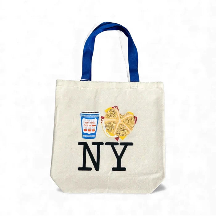 A large natural‑colored recycled‑cotton tote featuring a playful illustration of a classic New York breakfast: a blue‑and‑white Greek‑style coffee cup and a bacon, egg, and cheese sandwich on a speckled round yellow roll. The bag is roomy with a flat bottom, long shoulder blue straps, and is designed for everyday carrying. It measures 16 inches wide by 15.5 inches tall, has a 6‑inch gusset, and is machine washable in cold water.