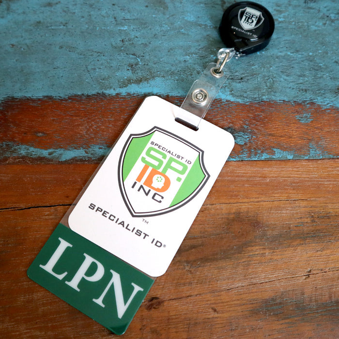 A badge labeled "SPECIALIST ID INC" and "LPN" with a retractable reel is resting on a wooden surface, featuring Custom Printed Clear Badge Buddies Vertical (Standard Size) - Customize with Title and Color for instant role recognition.