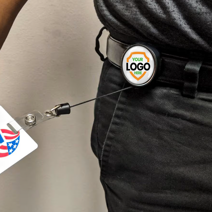 A person wearing a Customizable Key-Bak Mid Size ID Badge Reel with Steel Belt Clip (6ID) - Upload Your Logo, featuring logo customization, holding an ID badge with a partial American flag design.