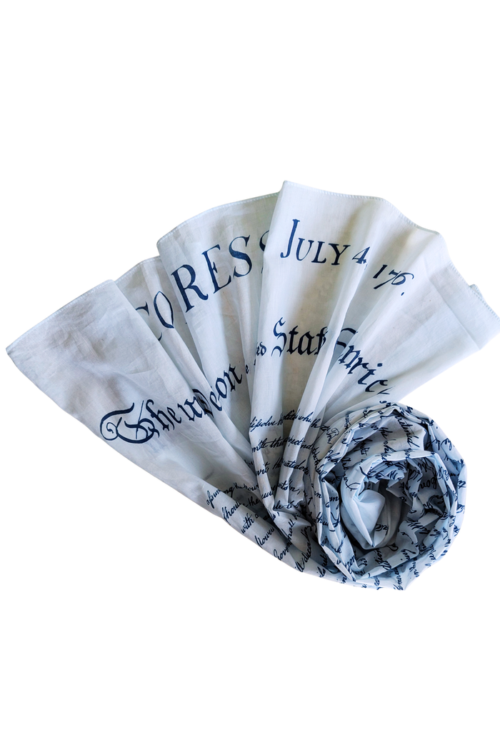 This lightweight rectangular scarf is soft and smooth with a slightly linen‑like texture. It is beige, resembling aged parchment, and printed in black with the opening text of the U.S. Declaration of Independence, including “IN CONGRESS, JULY 4, 1776.” The text appears toward one or both ends, allowing it to be felt lightly through the fabric when draped or wrapped.