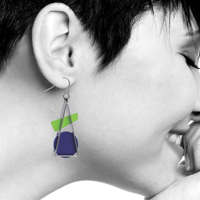Profile view of a model with a pixie haircut wearing Triangle at Rest earrings. The black-and-white photograph highlights the colorful geometric drop earrings, inspired by Wassily Kandinsky's abstract art, featuring open silver-plated brass shapes with a prominent triangle framing a blue-green acrylic accent.