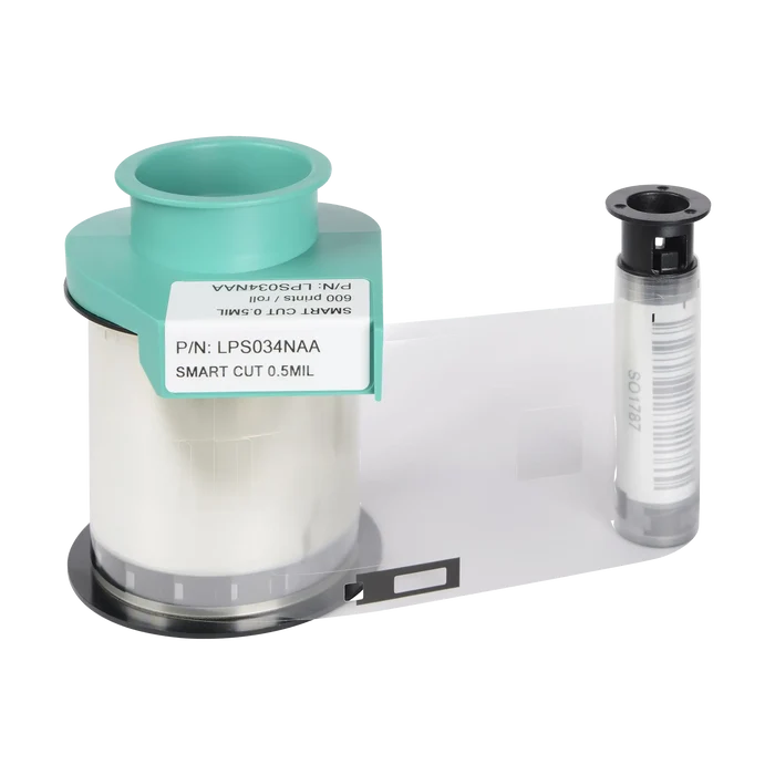 On a white surface, a roll of clear patch lamination ribbon with a teal spool and an attached label sits next to a small cylindrical black and gray component. The Evolis LPS034NAA Clear Smart Cut Patch Lamination, compatible with Primacy, Primacy2, and Avansia Lamination ID Card Printers, ensures high-quality results for your ID card printing needs.