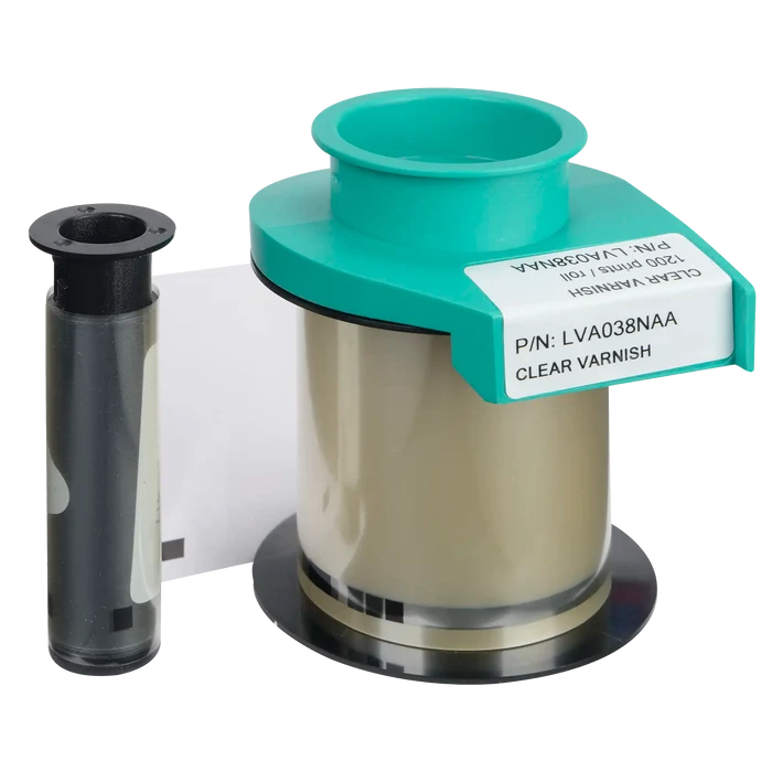 Next to an empty black plastic spool sits the Evolis LVA038NAA Clear Varnish Ribbon, distinguishable by its green and white label. This product, compatible with Primacy2 and Avansia Lamination, provides a protective layer for ID cards and can produce up to 1200 prints, making it ideal for use in ID card printers.
