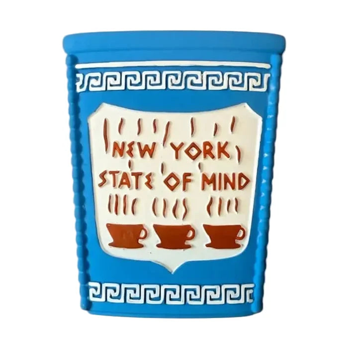 A product photo of a baby teething toy made from flexible, light-blue natural rubber. The toy is molded to look exactly like a miniature version of a classic New York City bodega coffee cup. It features a  decorative dark-blue Greek meander patterns across the top and bottom. In the center, the iconic 'New York State of Mind' slogan is written in a stylized Greek font in brown with 3 brown coffee cups below.