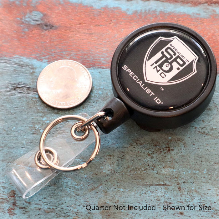 Heavy Duty Badge Reel w/ Metal Swivel Belt Clip & Key Ring with Specialist ID branding next to a quarter for size comparison. Featuring a metal swivel belt clip, this badge reel ensures secure attachment. Text at the bottom reads "Quarter Not Included - Shown for Size.