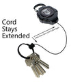 A Heavy Duty Retractable Ratchit Keychain Tether Reel for Multiple Keys with Clip and Locking Feature with a black case and extended Kevlar cord holding a set of five keys. Text reads: "Cord Stays Extended" and "Cable Stays Slack Until Pulled Again.