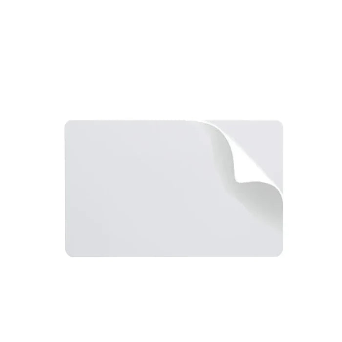 A rectangular white Fargo 81759 UltraCard 10 mil PVC card with a peeled corner that reveals a subtle curl and its adhesive backing. The background is plain white.
