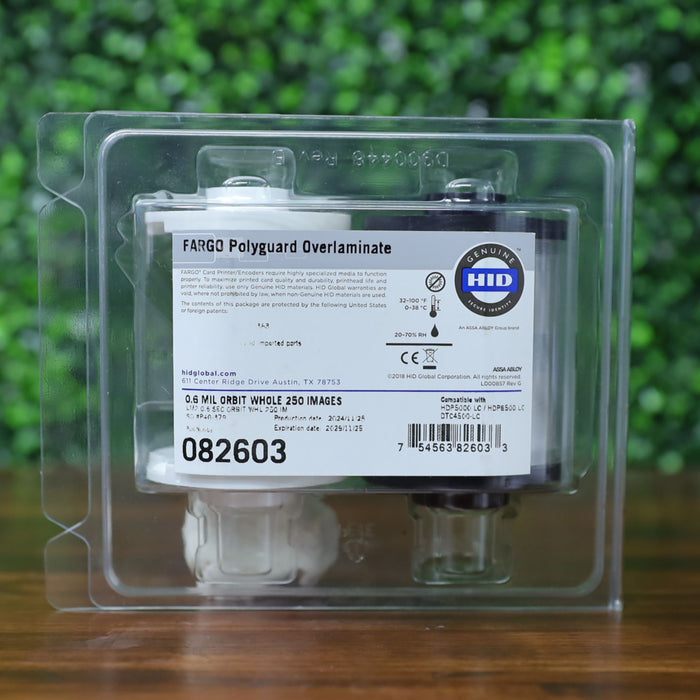 "Front-facing view of the HID Fargo 82603 PolyGuard Overlaminate in sealed clamshell packaging with label showing 0.6 mil orbit design and 250 image yield. Photographed and sold by Specialist ID, an authorized Fargo dealer.