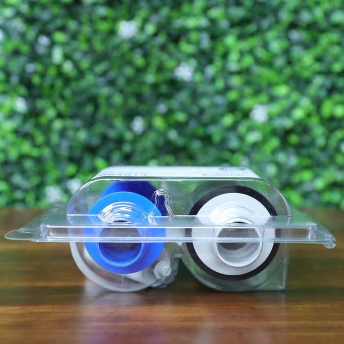Bottom view of the HID Fargo 84514 YMCFK ribbon lying flat inside its sealed clamshell packaging. Blue and white spools are clearly visible through the transparent plastic with the white cleaning roller nested between. Photographed and sold by Specialist ID, an authorized HID Fargo dealer.