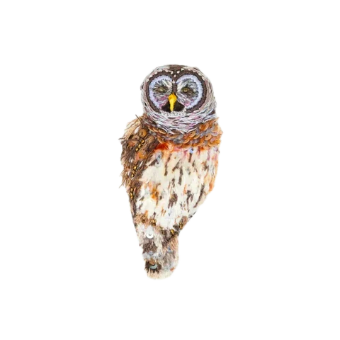A close-up of a Hoot Owl (Great Horned Owl) brooch set against a plain background. The small owl has a rounded body in warm browns, with a cream breast delicately speckled in orange and brown. Its lilac head is upright and forward-facing, highlighting a petite yellow beak. Fine hand embroidery creates a richly textured, raised surface, giving the feathers a soft, plush appearance with subtle depth and dimension.