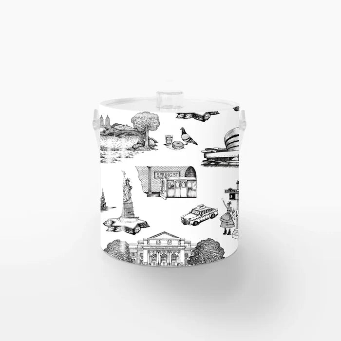 Ice Bucket: New York Toile: The bucket has a white background with a bold black toile pattern showing simple line drawings of NYC icons—pigeons, bagels, Greek coffee cups, and yellow cabs—repeated evenly around the surface. It’s smooth, cylindrical, and topped with a snug lid and a handle in clear Lucite.