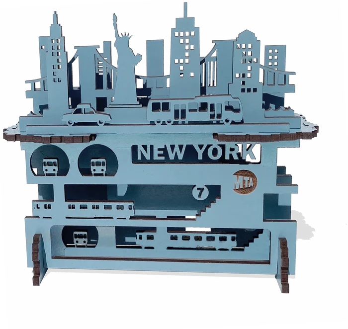 A layered wooden piece with a white background and raised blue shapes you can feel by touch. Smooth, thin wood forms New York City above and below the streets—buildings and landmarks on top, subway lines beneath—stacked to show the city’s depth and motion.