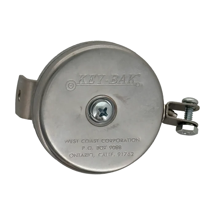 The Key-Bak #481LS-HD Mountable Retractable Reel, featuring a round, silver design with the brand name "KEY-BAK" and manufacturer details engraved on the front, includes a steel cable and comes with an L bracket and hex nut yoke. This heavy-duty key reel is ideal for industrial applications.