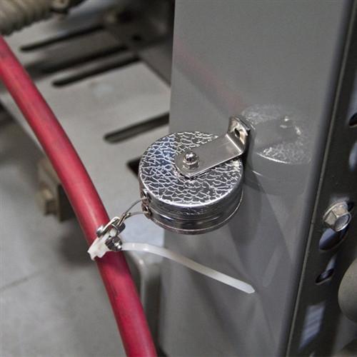 A Key-Bak #481LS-Twin Industrial Dual Retractable Reel with 48" Steel Cable attached to a vertical metal surface, with a red cable and plastic zip tie nearby. Sold by Specialist ID.