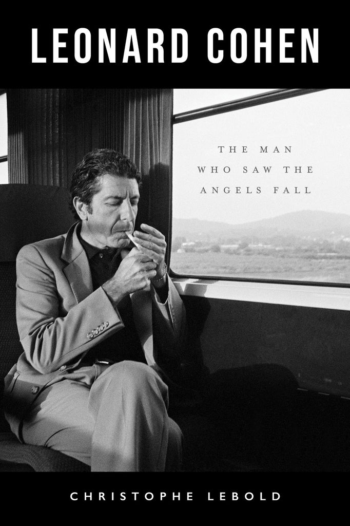 Book title: Leonard Cohen: The Man Who Saw Angels Fall. The cover shows a close-up black‑and‑white photograph of Leonard Cohen seated beside a train window, lighting a cigarette. Outside the window, a soft, light‑grey pastoral landscape drifts by. The title appears in large white letters, with the subtitle in smaller black text placed on the window.