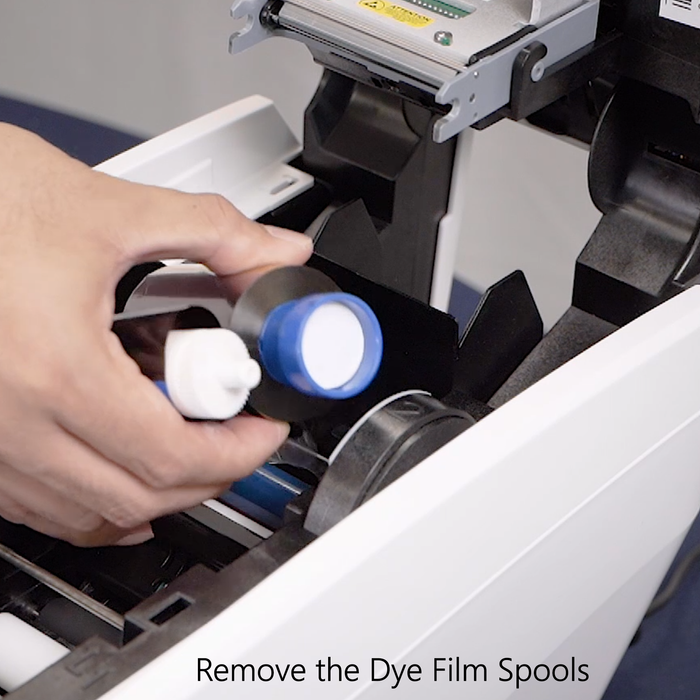 Person removing dye film spools from a printer with text 'Remove the Dye Film Spools'. Sold by Specialist ID.