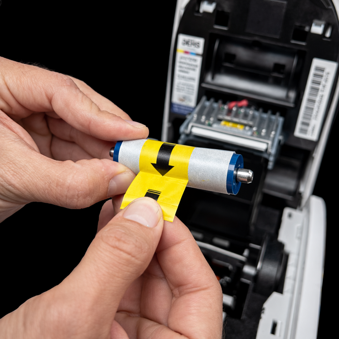 Person holding a small cylindrical cleaning roller with warning tape in front of an open printer. Sold by Specialist ID.