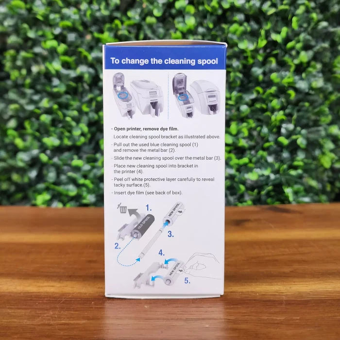 The Magicard MA1000K-Black Monochrome K Ribbon - 1000 Prints packaging features illustrated, step-by-step ribbon change instructions on a leafy green background and wood surface—ideal for your monochrome ID card printing needs.