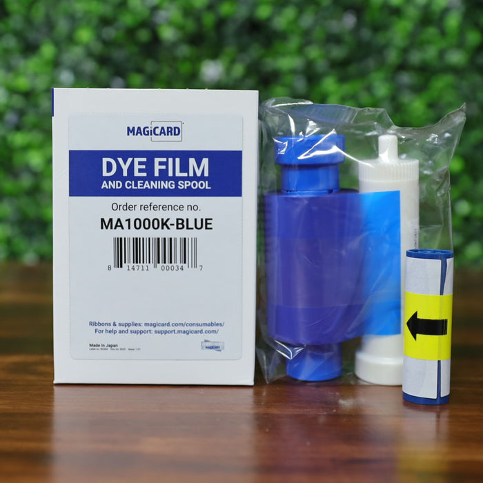 Magicard MA1000K-Blue ribbon cartridge with cleaning spool and cleaning solution in retail packaging on wood surface with green foliage background. Photographed and sold by Specialist ID, an authorized Magicard dealer.