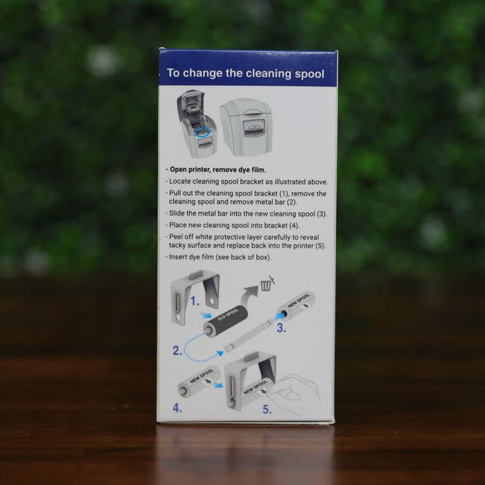 Side of Magicard MA1000K-Scratch scratch-off ribbon box showing step-by-step illustrated instructions for replacing the cleaning spool, with text and diagrams, displayed on a wood surface with green leafy background, photographed and sold by Specialist ID, an authorized Magicard dealer.