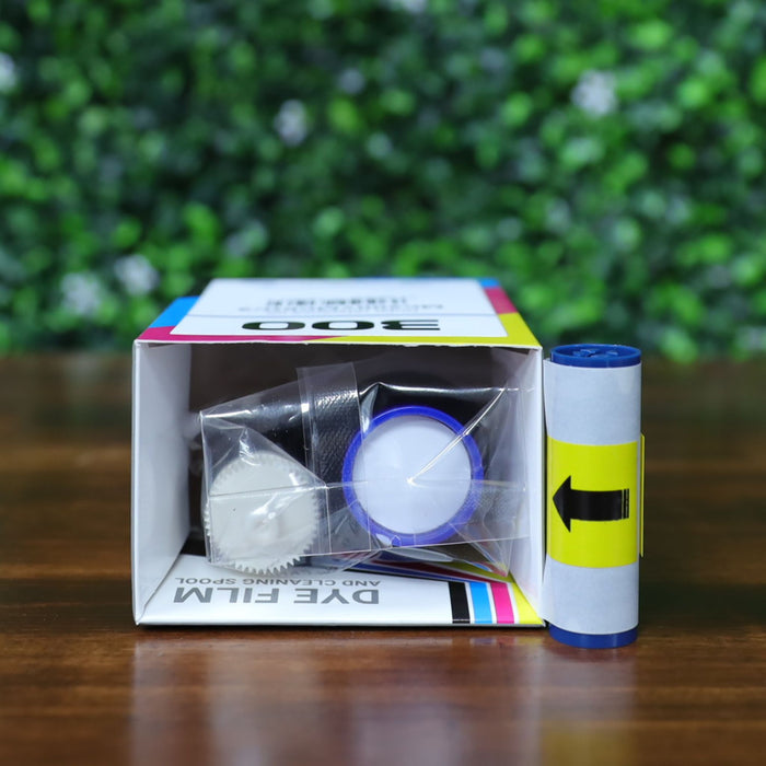 Top-down view of Magicard MC200YMCKO/2 ribbon kit showing interior packaging with ribbon spool, cleaning roller, and plastic wrap inside the branded box. Includes separate cleaning roller placed upright for display. Photographed and sold by Specialist ID, an authorized Magicard dealer.