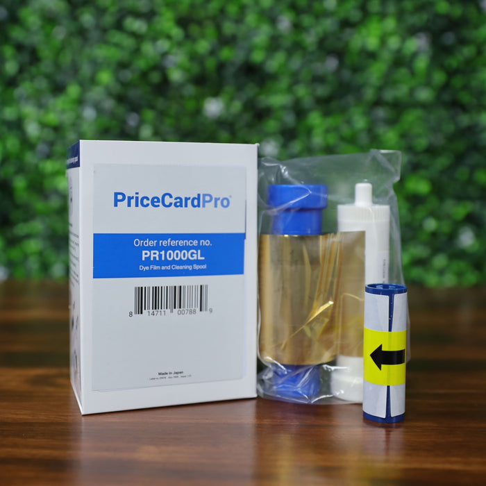 A Magicard PR1000GL Monochrome Gold Ribbon (1000 prints), compatible with PriceCardPro 100 and Flex+ ID card printers, is displayed on a wooden surface with a green patterned background—ideal for printer maintenance. Photographed and sold by Specialist ID, an authorized Magicard dealer.