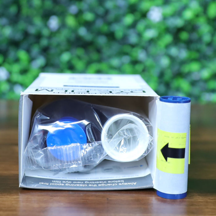 Top-down view of the Magicard PR300COL YMCKO ribbon kit with the box lying face down and opened to reveal the sealed dye ribbon, cleaning spool, and adhesive roller inside. Photographed and sold by Specialist ID, an authorized Magicard dealer.