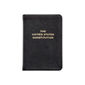 A black, leather‑bound book titled The United States Constitution, with the title stamped in gold lettering, shown against a clean white background.