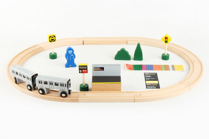 The image shows the contents of the New York City Subway 20‑Piece Wooden Subway Set displayed with the pieces arranged for play: two subway cars, wooden tracks, a platform, a conductor figure, trees, and several signal signs.