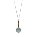 On a white background, the necklace displays an ornate magnifying glass pendant made of aged brass. The magnifying glass is about four inches long, with a decorative handle and a clear, working lens. It hangs from a matching aged brass scroll chain and closes with a small lobster clasp, giving the piece a refined, antique-inspired appearance.