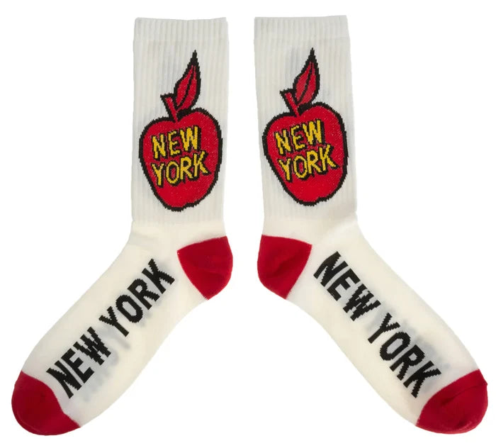 These white socks feature a bold red cartoon apple outlined in black, with “New York” written across it in yellow letters edged in black on the leg. The heel and toe are solid red, while “NEW YORK” appears in bold black text along the white foot. Made from a soft, stretchy blend of cotton, nylon, and elastane, they are machine washable and designed as one size fits most.